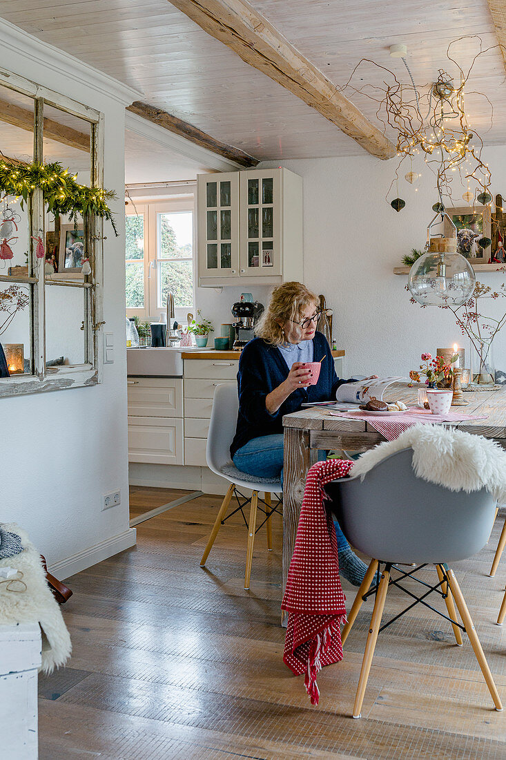 Woman reading magazine in wintry dining room adjoining country-house kitchen
