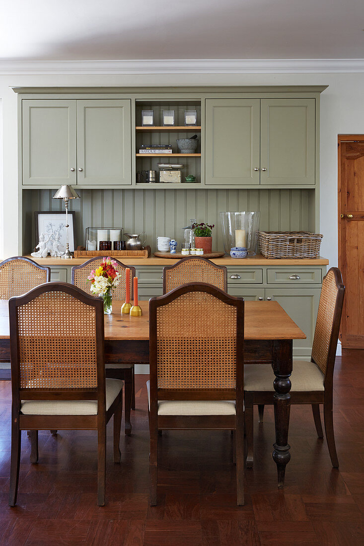 Grey-green dresser and cane-backed chairs around dining table in kitchen-dining room