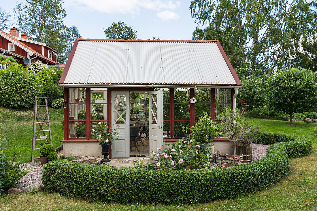 Rotes Gewächshaus im sommerlichen Garten