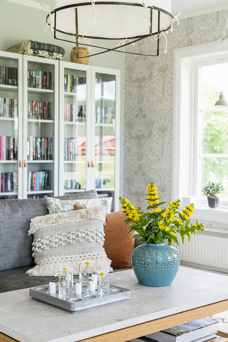 Blue vase of yellow loosestrife and glass-fronted bookcases in living room