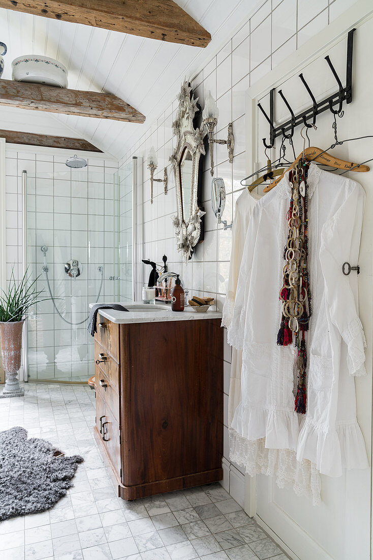 White tunics hanging from row of hooks and wooden ceiling beams in bathroom decorated in Boho style