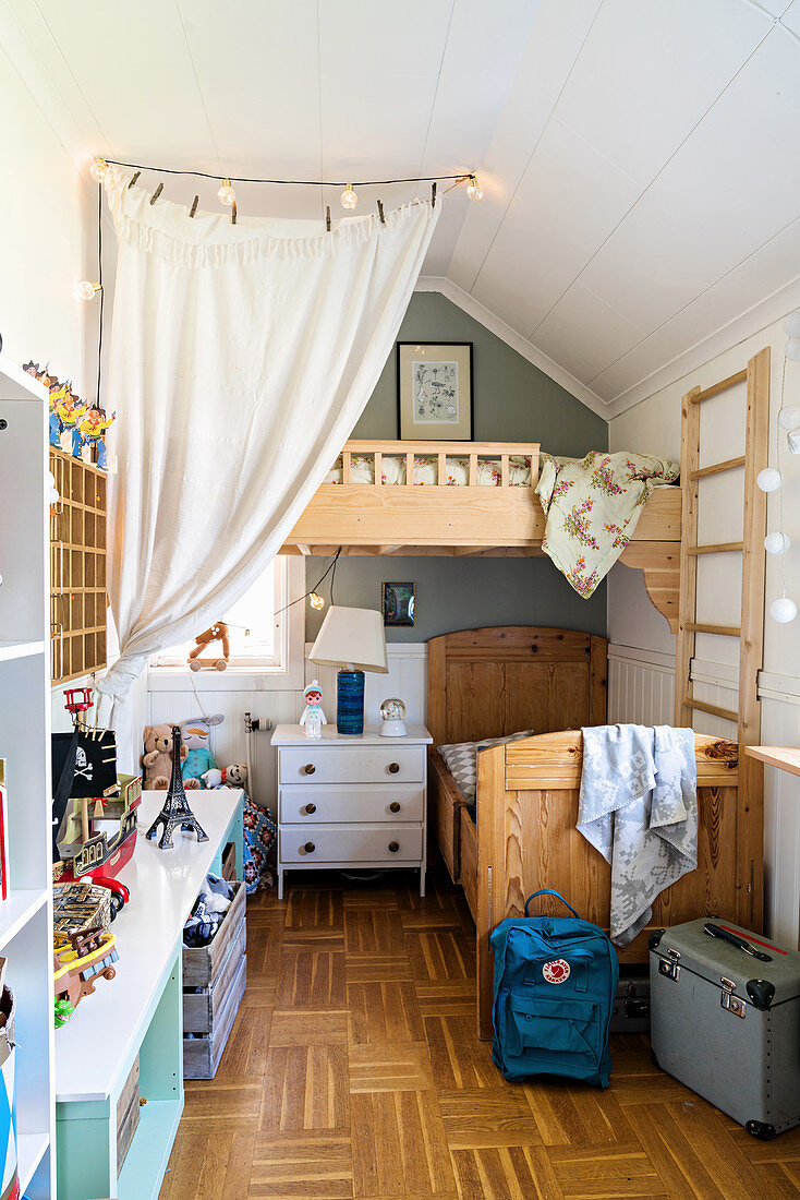 Wooden bed and chest of drawers below loft bed in siblings' bedroom