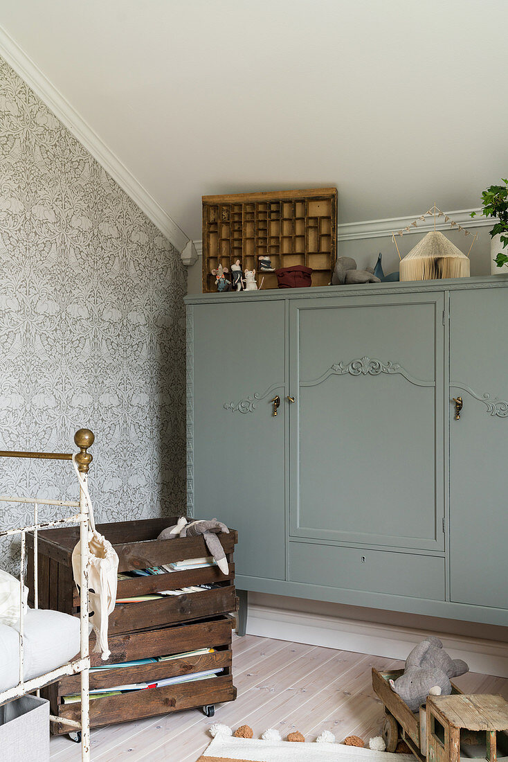 Antique grey cabinet in child's bedroom with patterned wallpaper