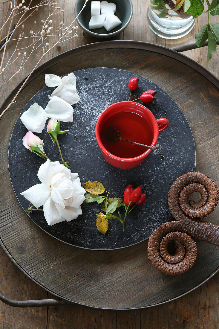 Rote Teetasse dekoriert mit Hagebutten, Rosen und Widderzapfen