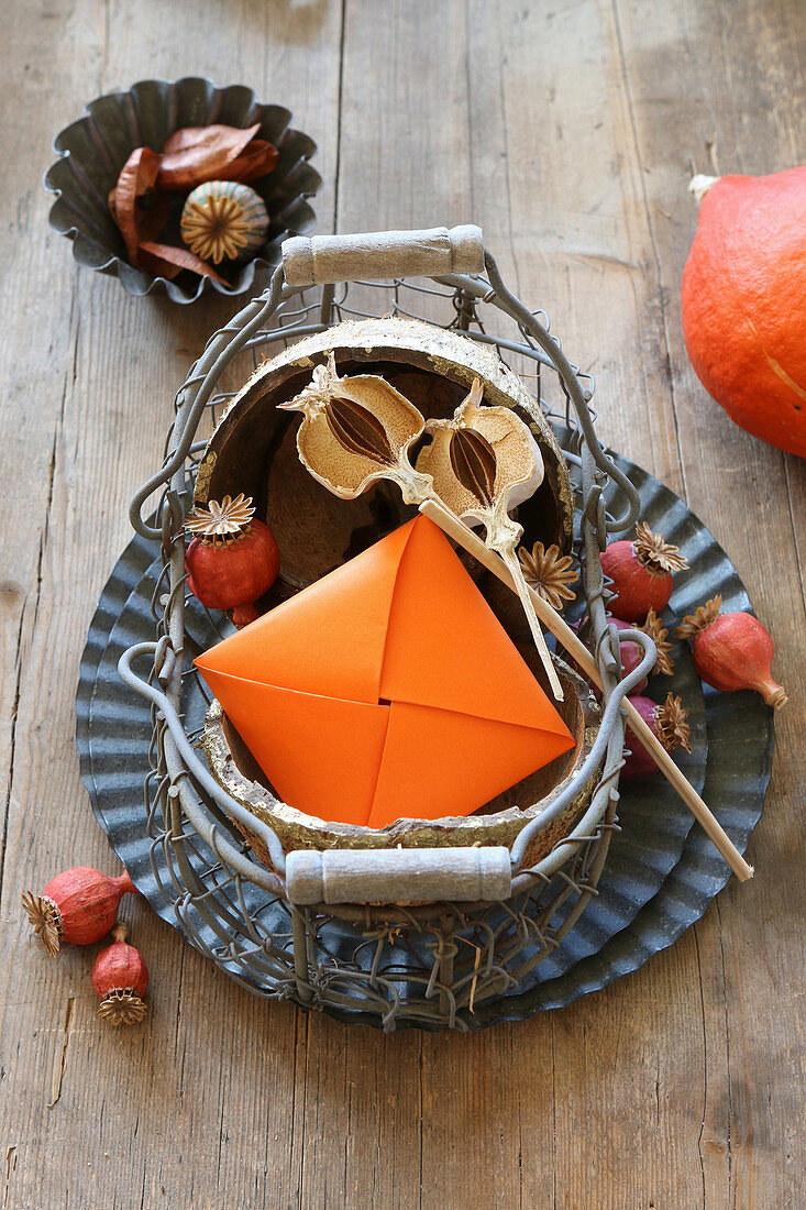 Herbstdeko mit Mohnkapseln und Origami-Briefumschlag im Drahtkorb
