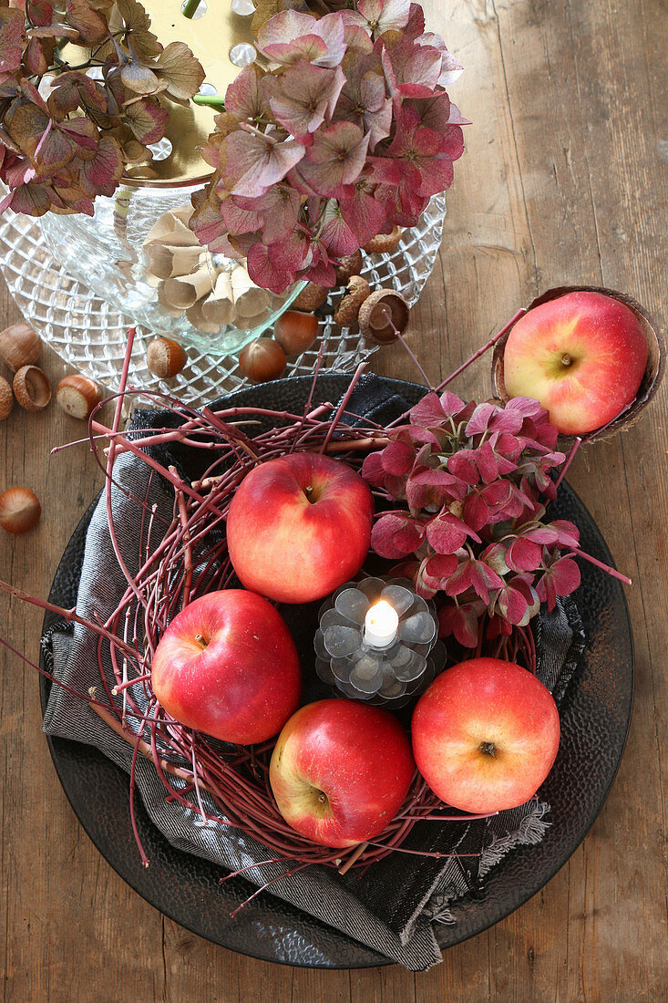Herbstliche Tischdeko aus Äpfeln, Zweigen, Hortensienblüten und Kerze