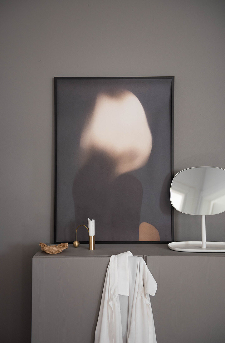 Modern artwork, mirror and candle on grey cabinet