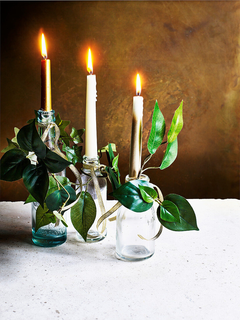 Weihnachtliche Tischdeko: Flaschen mit Kerzen, Blättern und Goldband