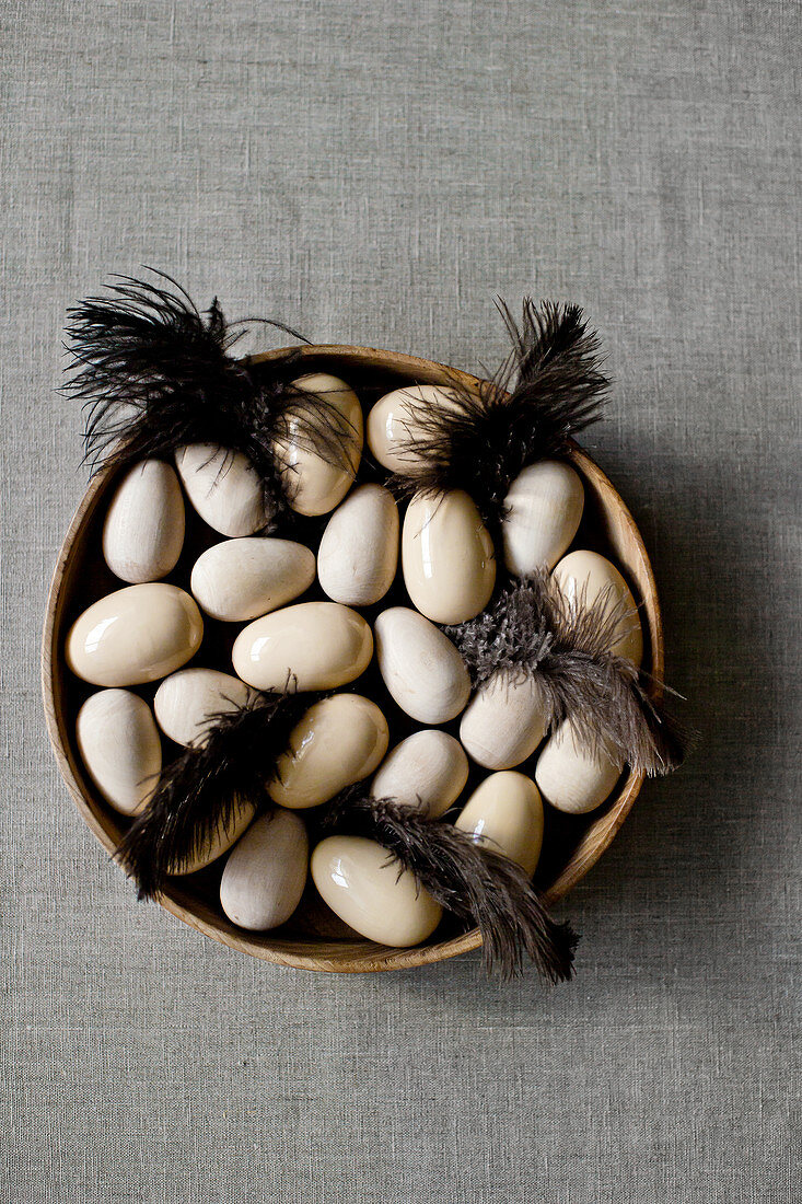 Eier aus Holz und Keramik und braune Federn in einer Holzschale