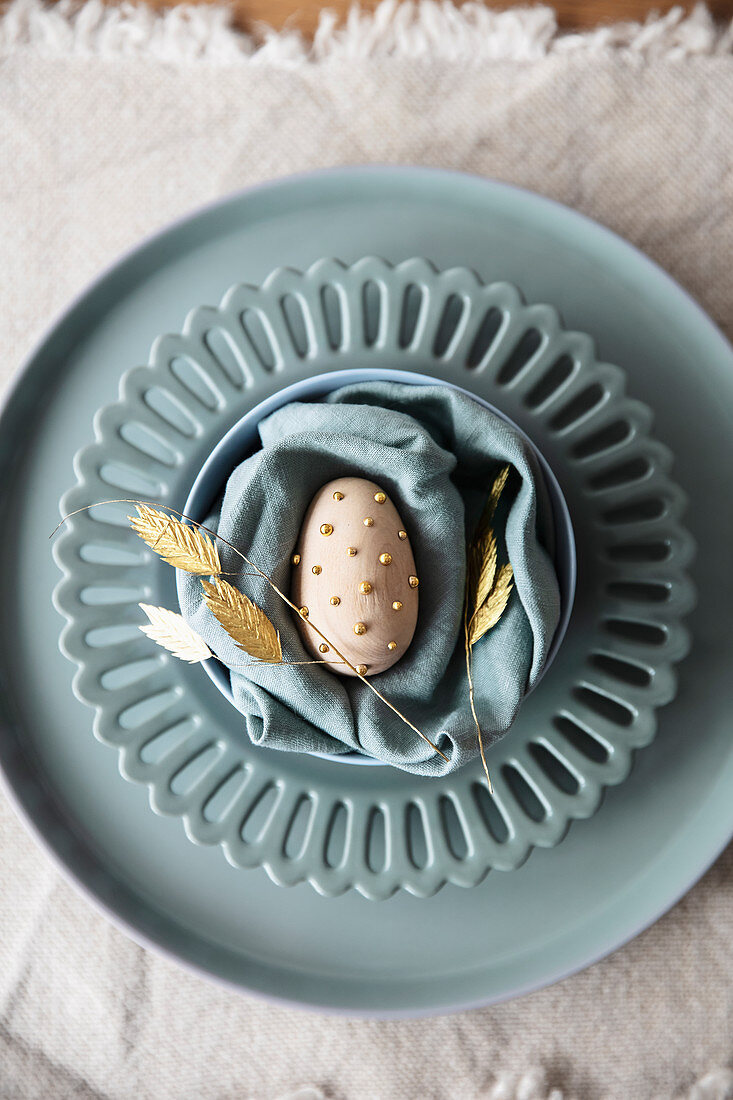 Egg with golden beads on blue-grey plate and napkin