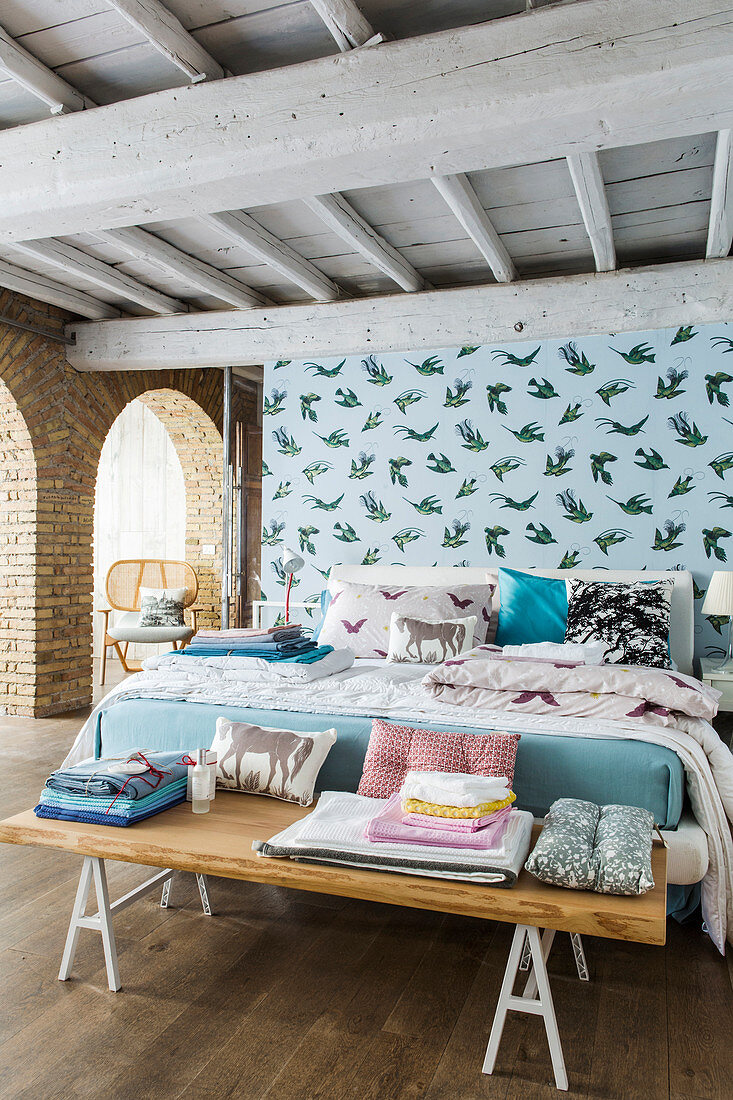 Double bed and bedroom bench in front of pale blue partition wall with pattern of birds