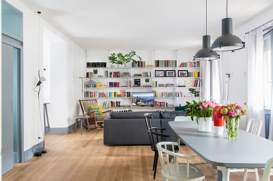Offener Wohnraum mit Esstisch und Sitzbereich mit Sofa und Schaukelstuhl vor Bücherwand