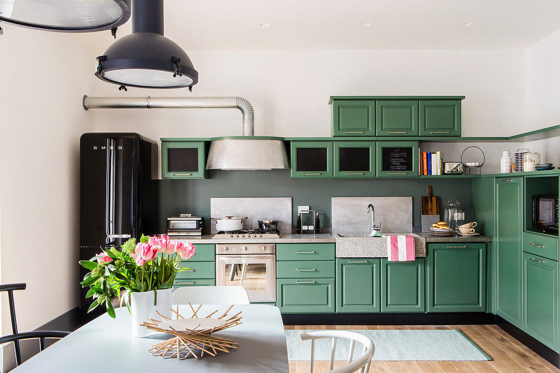 Green, country-house-style kitchen with industrial lamps over dining table