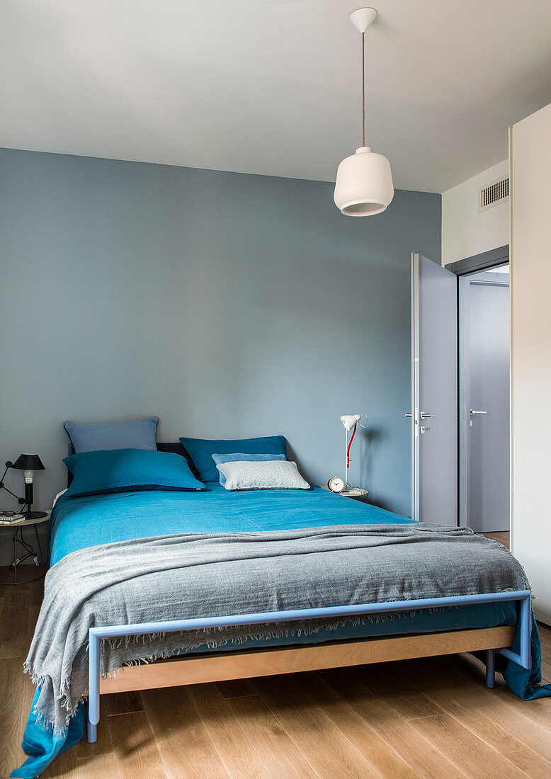 Bed with blue and grey bed linen in bedroom with blue-painted walls