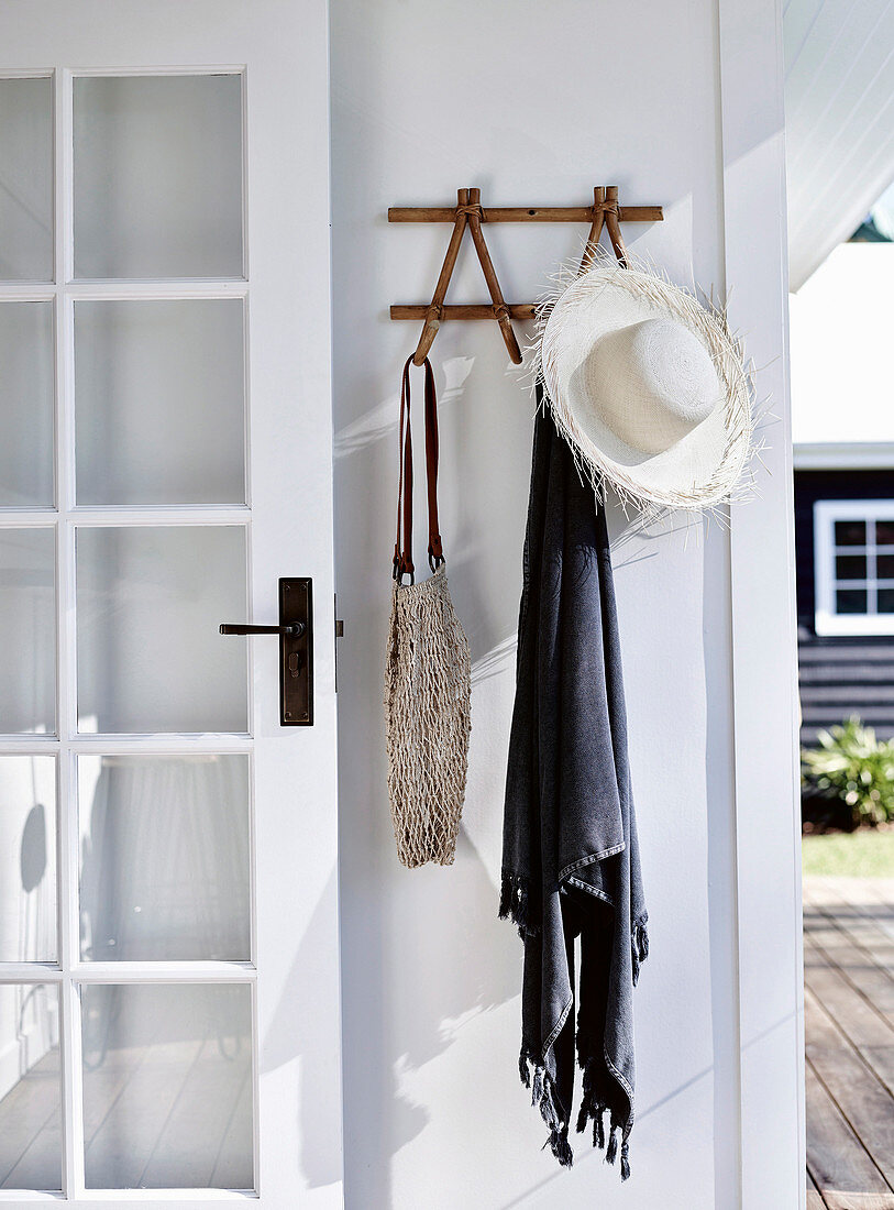 Garderobe mit Sonnenhut, Tuch und Tasche an weißer Wand, neben Sprossentür
