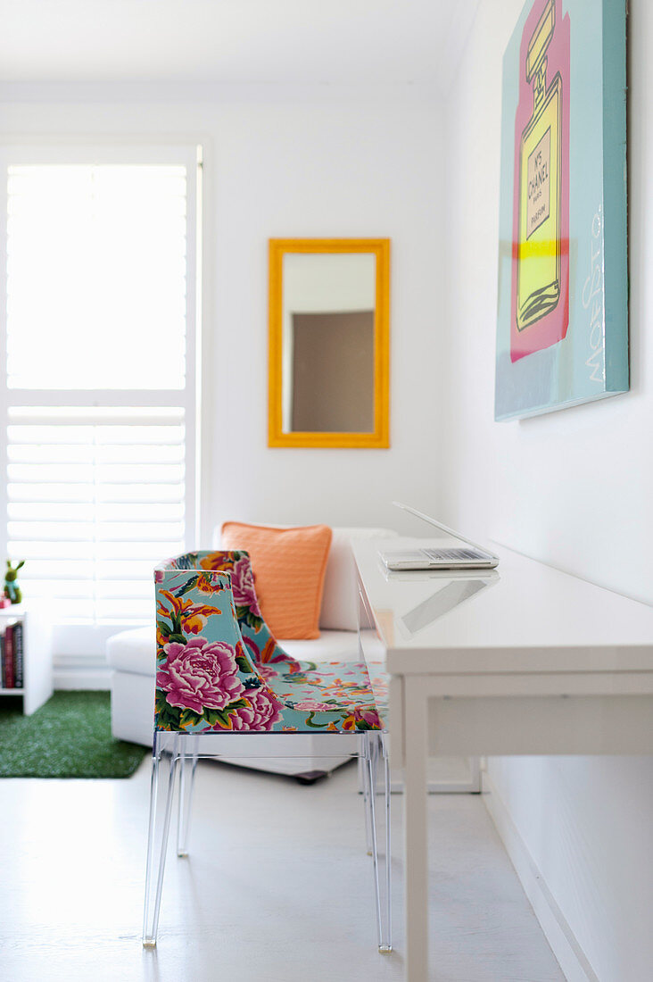 Schlichter, weißer Schreibtisch mit buntem Stuhl, Polstersessel und Wandspiegel