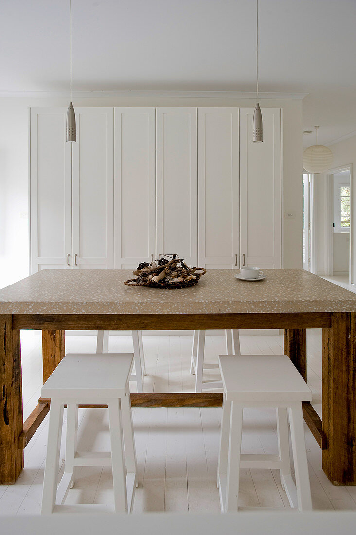 Wooden table with marble top and white stools in front of white cupboard