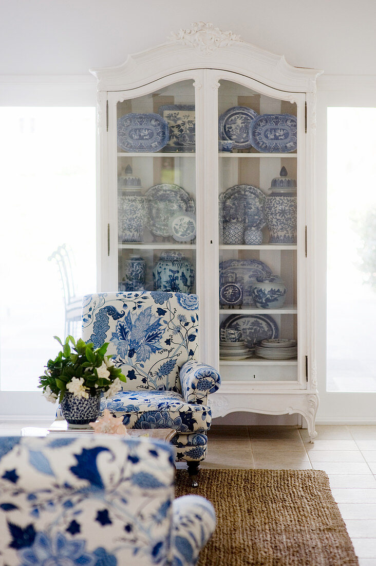 Sessel mit weiß-blauem Bezug vor weißem, antikem Geschirrschrank