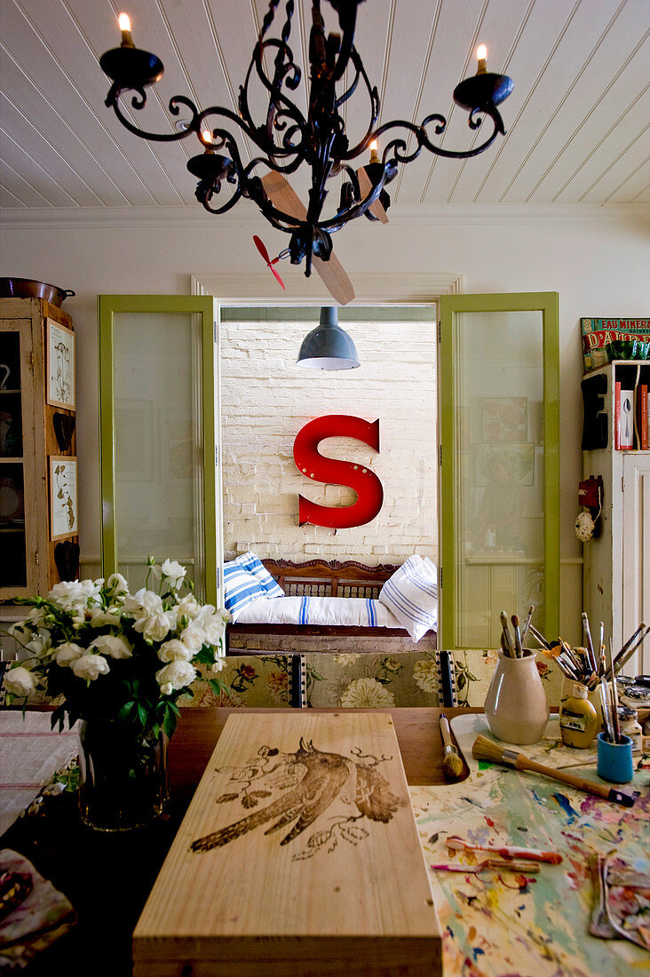 View across painting table to antique bench below large red letter S on brick wall