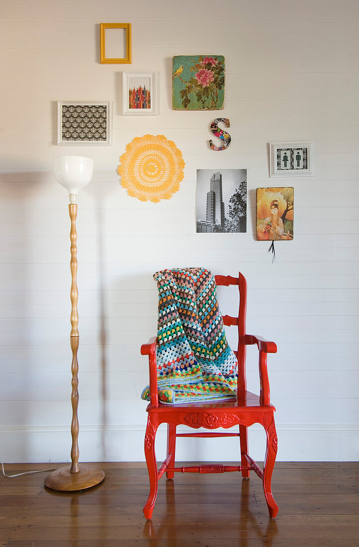 Roter Armlehnstuhl mit bunter Decke und Stehlampe vor weißer Wand mit Deko