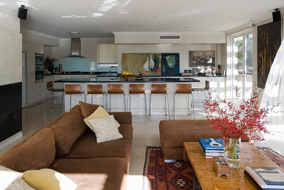 Wohnraum mit brauner Polstergarnitur im Sitzbereich und offener Küche mit Frühstückstheke