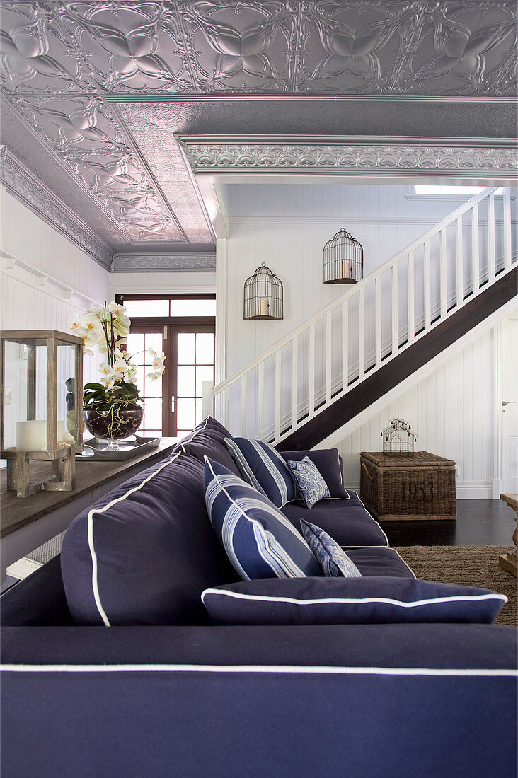 Blaues Polstersofa im Wohnraum mit Treppe und silberfarbener Stuckdecke