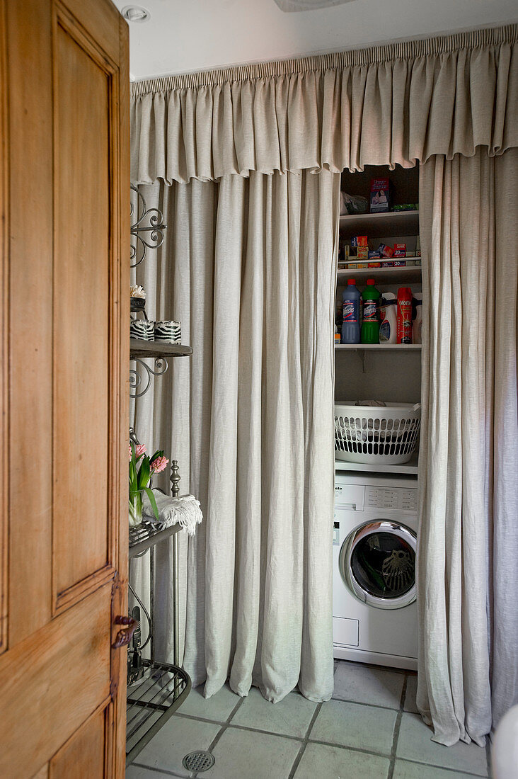 Washing machine and shelves hidden by floor-to-ceiling grey curtain