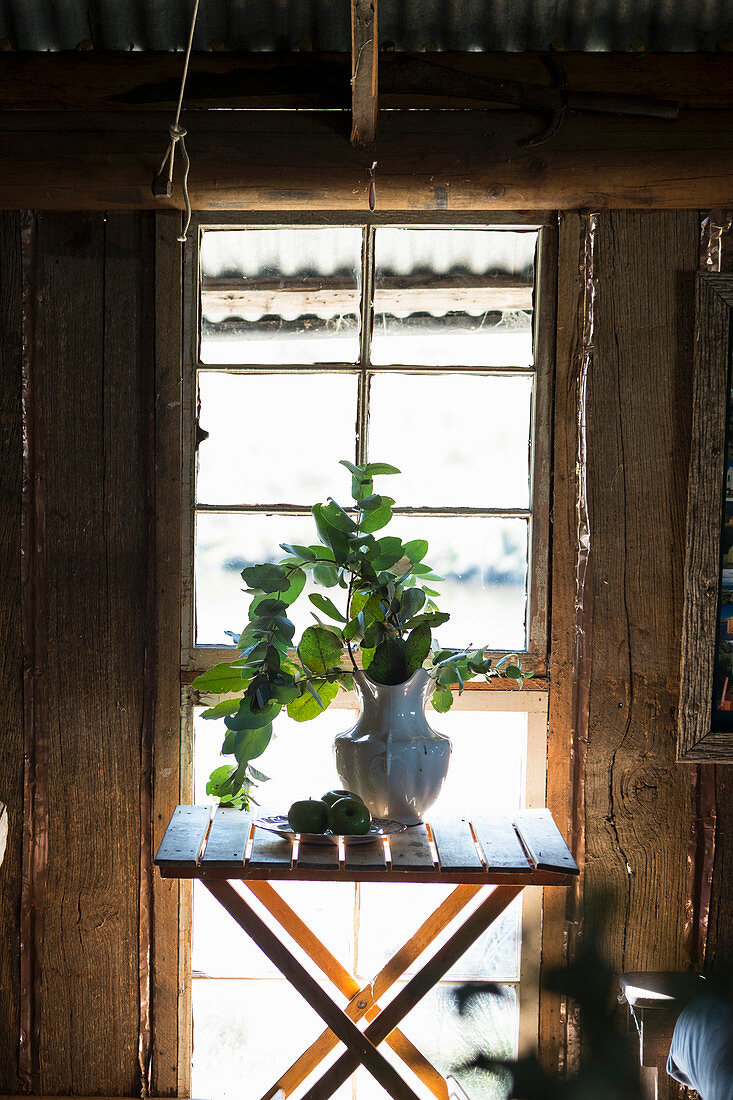 Vase of small folding table in front of window in rustic wooden cabin