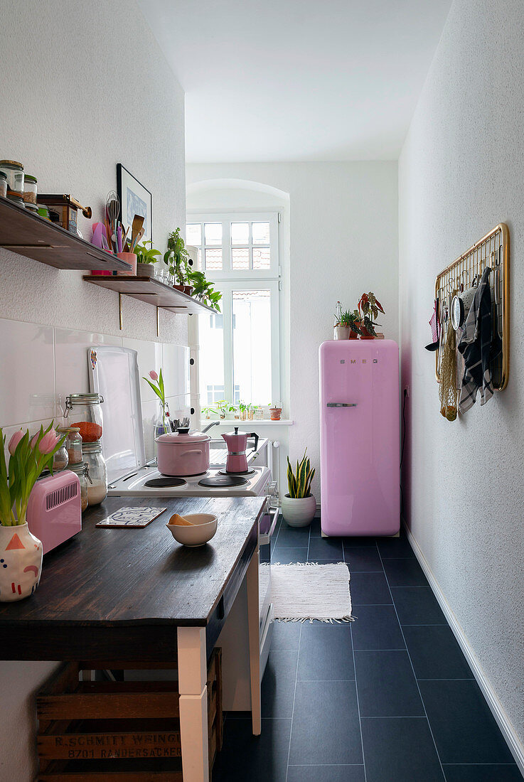 Schmale Küche mit dunklen Fliesenboden, im Hintergrund rosa Kühlschrank