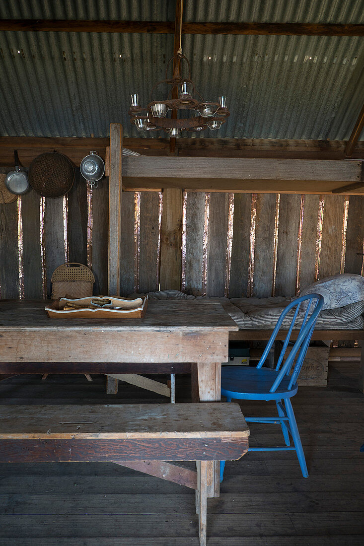 Einfacher Schlafplatz sowie Esstisch mit Stuhl und Bank in rustikaler Holzhütte