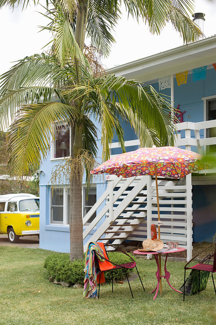 Zweistöckiges blaues Strandhaus mit Gartenmöbeln unter Palme