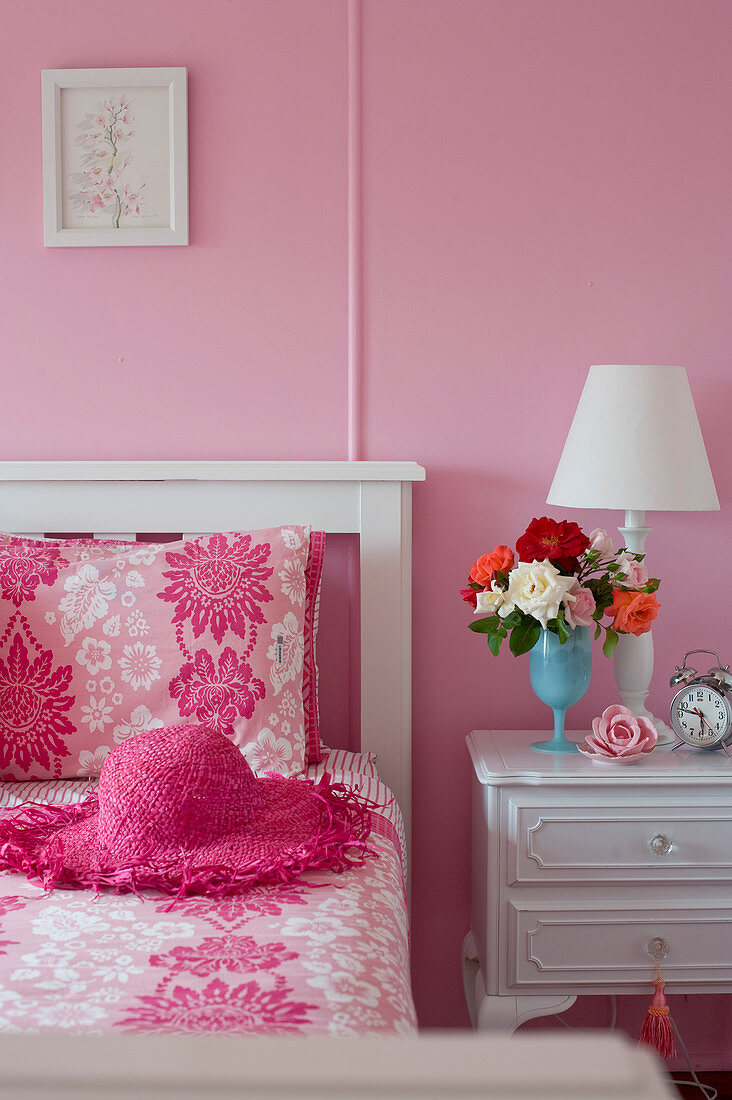 White wooden bed and white bedside cabinets in feminine, pink bedroom