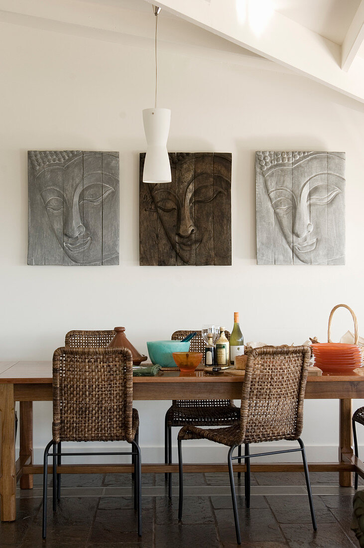 Three pictures of Buddha on wall above wooden dining table with wicker chairs