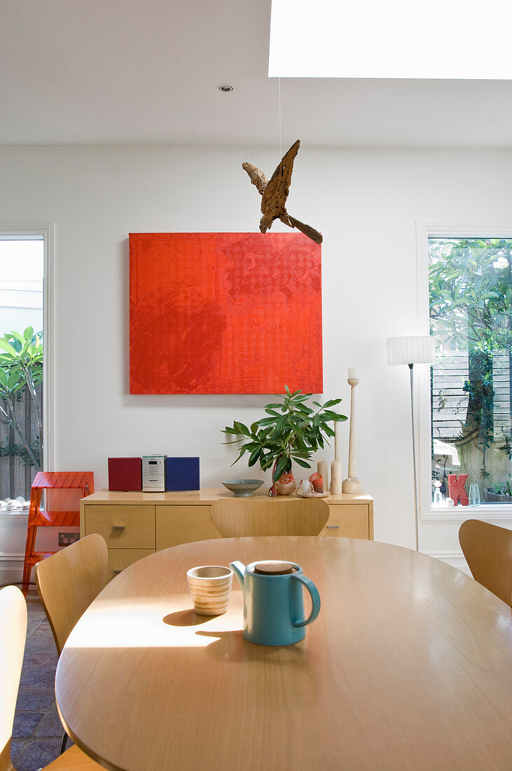Abstraktes Wandbild über Lowboard in Wohnraum mit ovalem Esstisch und Klassikerstühlen