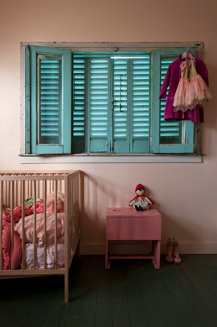 Vintage-Kinderzimmer in Rosa mit Gitterbett unter Fenster mit blauen Fensterläden