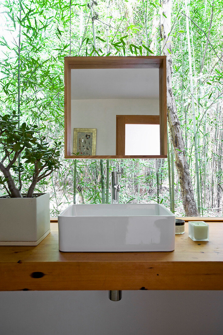 Waschtisch mit quadratischem Spiegel aufgehängt vor Fensterfront mit Blick ins Grüne