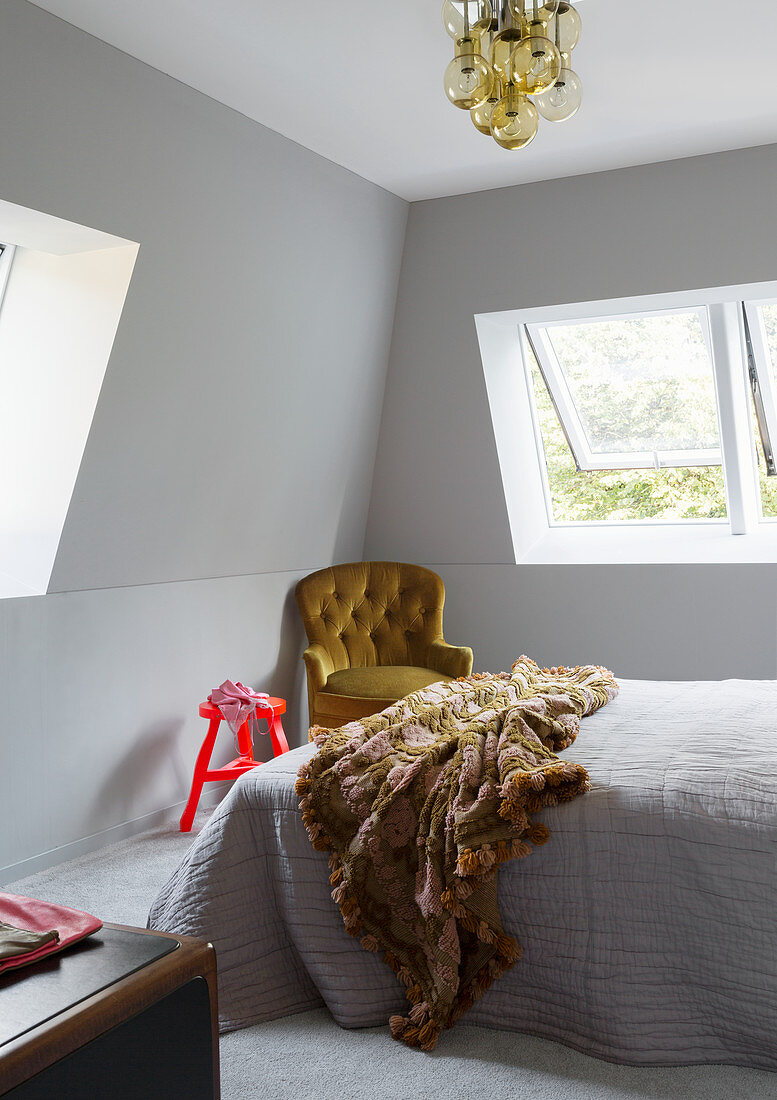 Doppelbett und Sessel im Schlafzimmer mit grauen Wänden und leichter Dachschräge