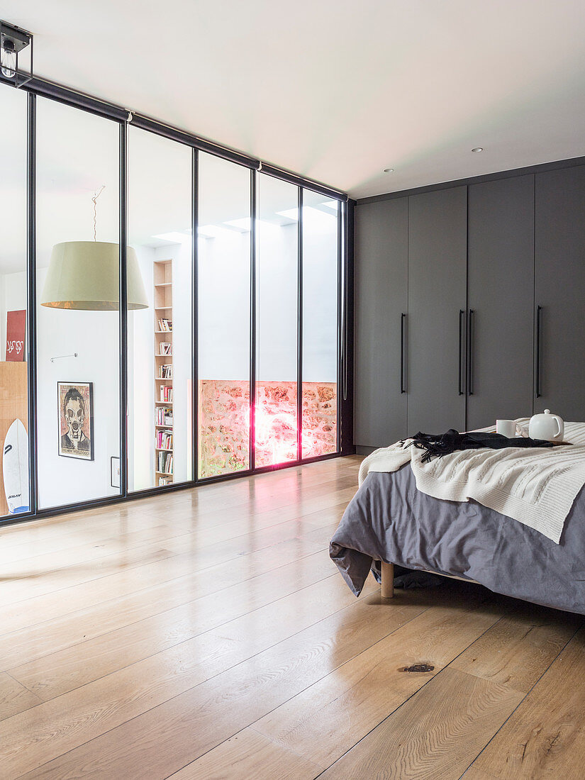Schlafzimmer im verglasten Galeriebereich mit Doppelbett und grauem Einbauschrank