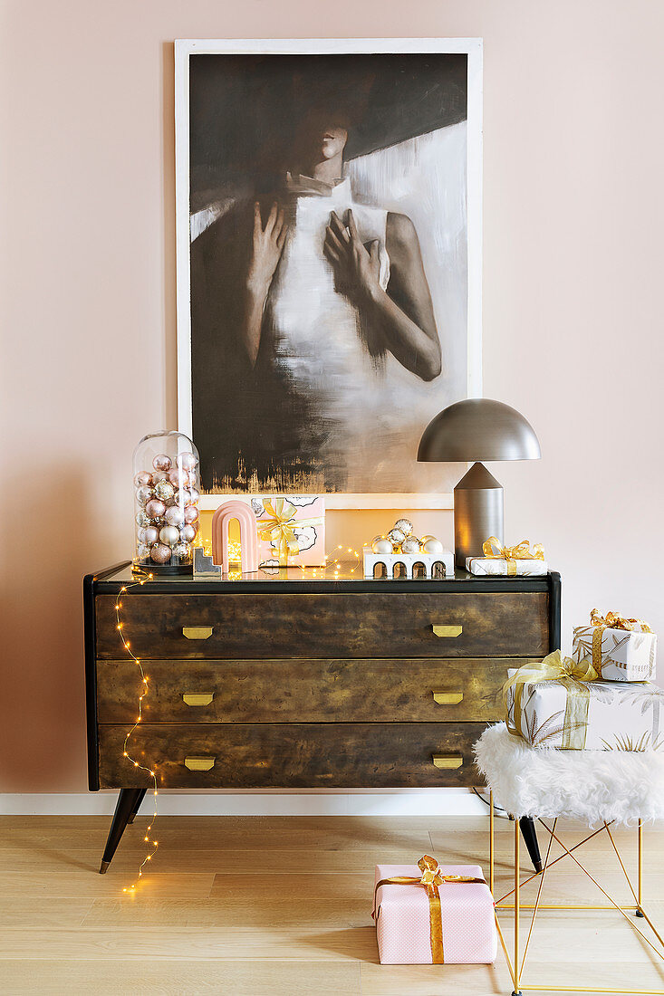Painting above dark chest of drawers with feminine Christmas decorations