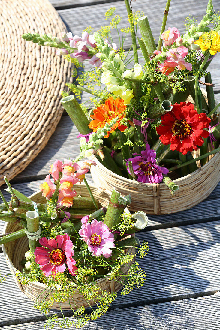 Gestecke mit Knöterich, Zinnien und Löwenmäulchen in Körben