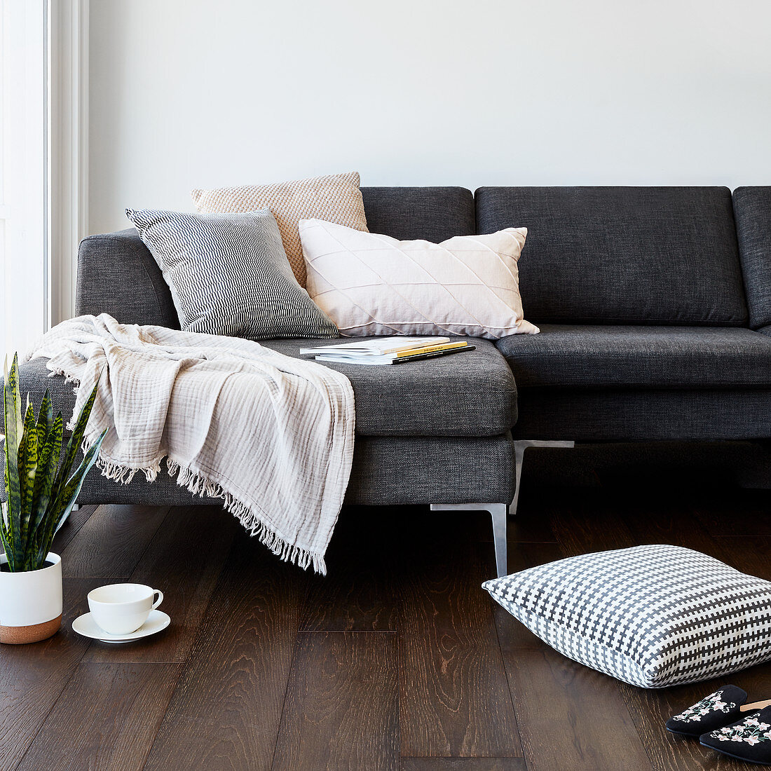 Kissen, Teetasse und Bogenhanf vorm grauen Sofa mit Plaid