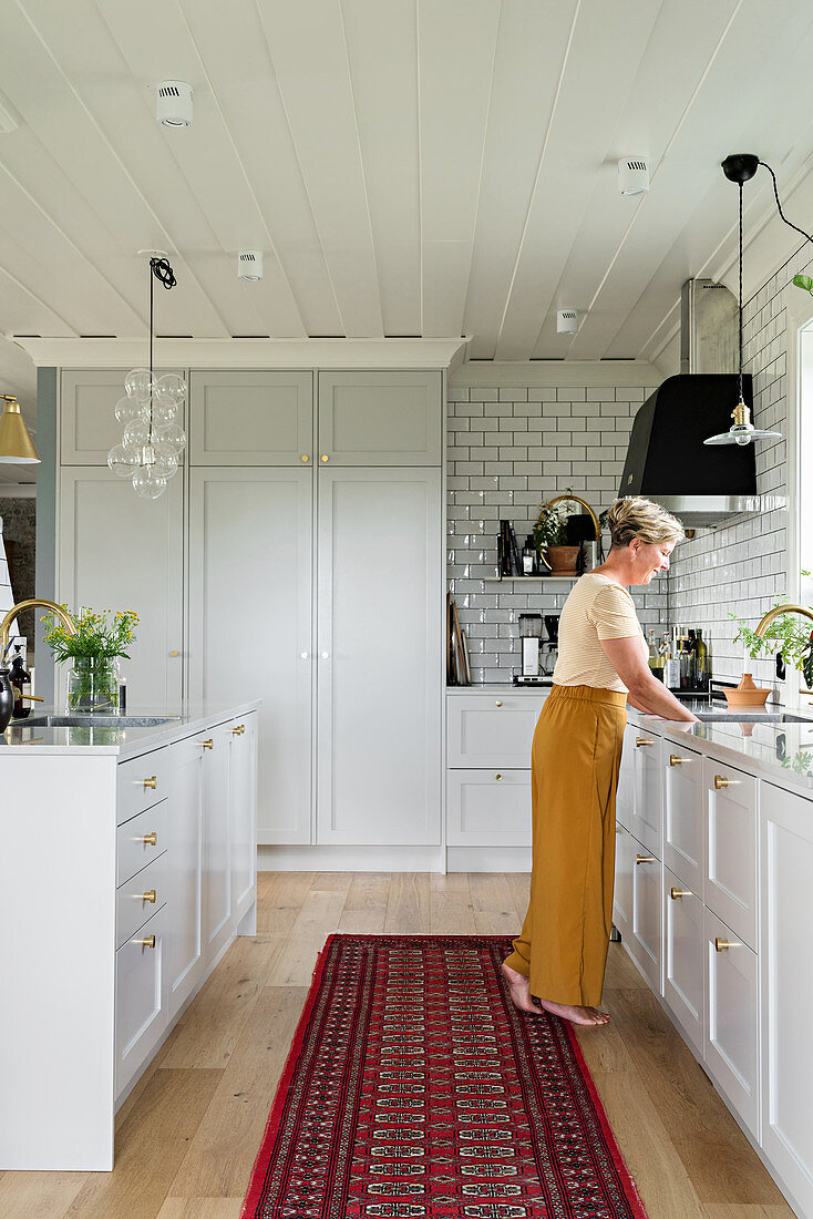 Woman in open-plan kitchen with elegant pale-grey panelled cabinets