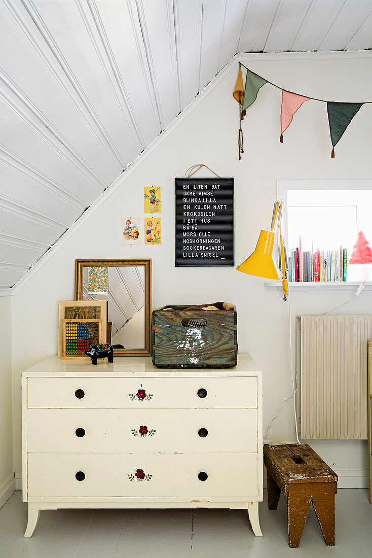 Old, white chest of drawers below sloping ceiling in child's bedroom