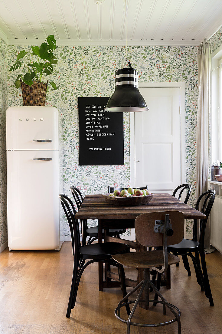 Black bistro chairs around table in dining room with floral wallpaper