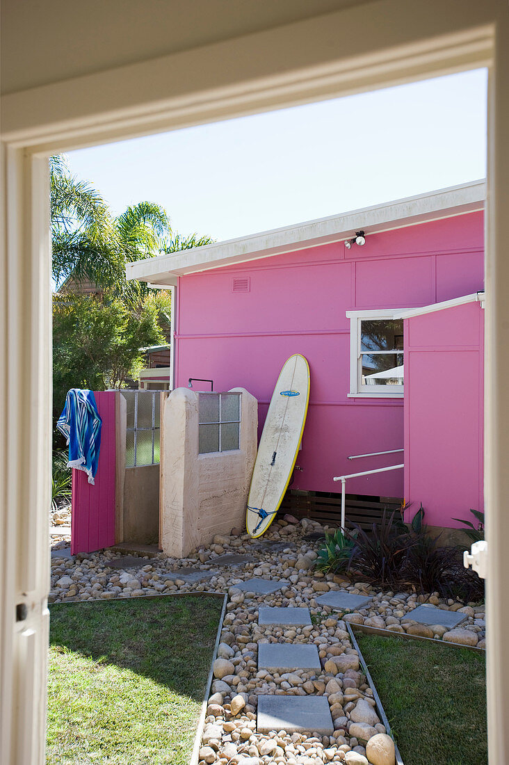 Pink house with outdoor shower and surfboard in garden
