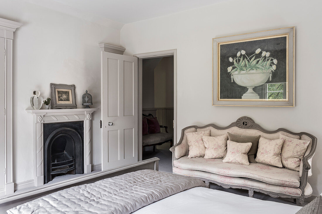 Victorian fireplace with reupholstered antique sofa below artwork in bedroom