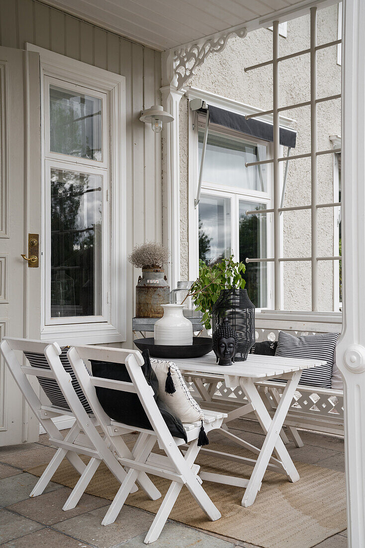 Weißer Holztisch mit Stühlen auf überdachter Veranda