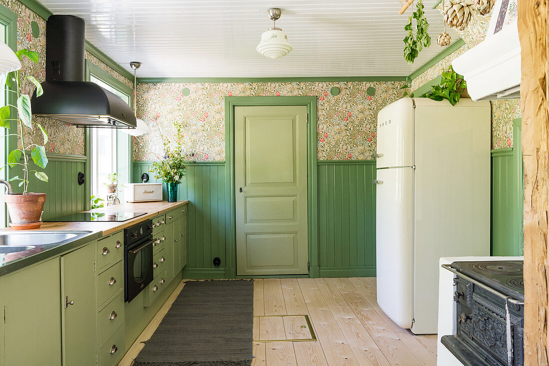 Green base units and nostalgic wallpaper in the kitchen