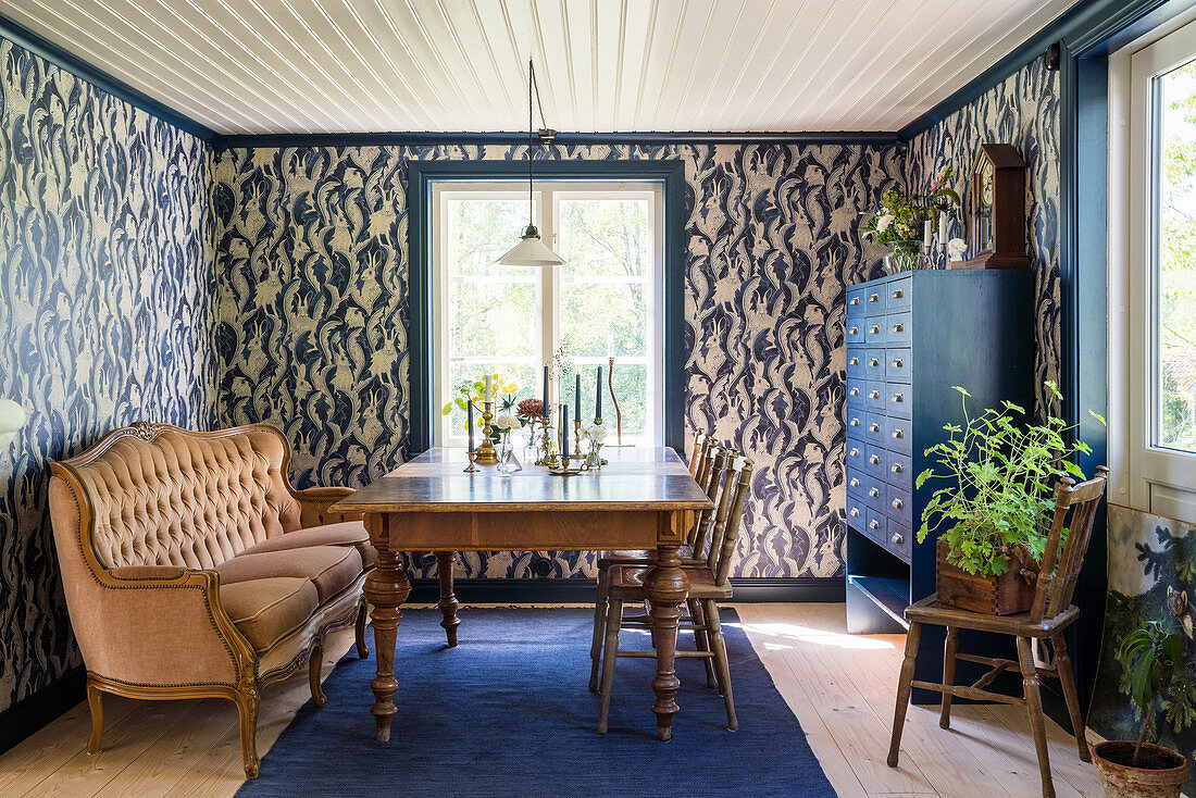 Antique wooden table, sofa and blue cabinet in dining room with patterned wallpaper