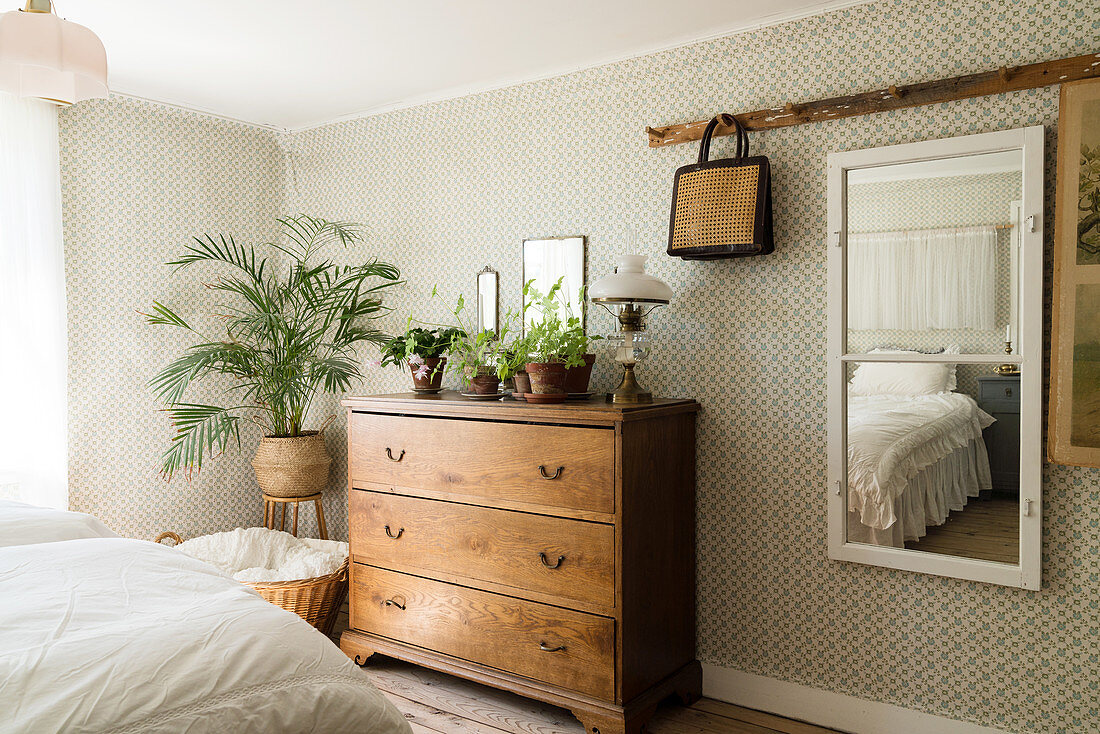 Wandspiegel, Holzkommode und Zimmerpalme im Schlafzimmer